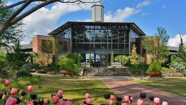 Un bâtiment moderne à la façade vitrée, entouré d’un jardin bien entretenu où poussent des tulipes.