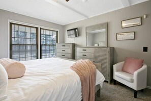 Un dormitorio con una cama grande, un aparador, una silla y un televisor en la pared.