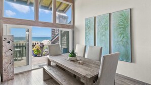 Ein Essbereich mit einem Holztisch, Stühlen und Blick auf den Strand durch große Fenster.
