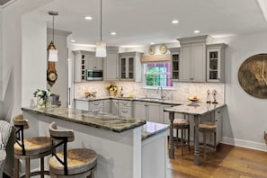 A kitchen with a central island, bar stools, and a large clock on the wall. - Pacific Serenade: Brand New Remodel (Carmel-by-the-Sea)