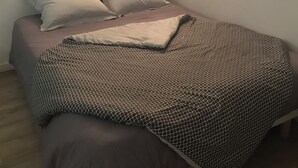 A single bed with a patterned blanket, a brick wall, and a shelf with candles. - Charming, renovated studio apartment in Toulouse, in a beautiful location (Toulouse)