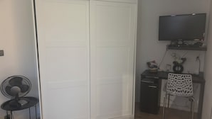 A room with a white wardrobe, a desk with a computer, a chair, a fan, and a television on a stand. - Charming, renovated studio apartment in Toulouse, in a beautiful location (Toulouse)