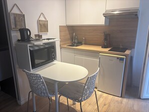 A compact kitchen with a microwave, stove, sink, and a small refrigerator. There is a white table with chairs and decorative items on the wall. - Charming, renovated studio apartment in Toulouse, in a beautiful location (Toulouse)