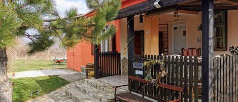 A cozy outdoor seating area with a wooden bench and stone steps leading to a house with a red roof and a black fence.