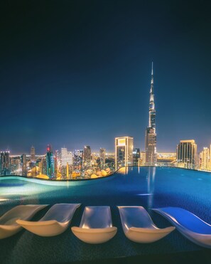 A rooftop pool with lounge chairs and a cityscape view at night, including a prominent skyscraper. - Paramount Hotel Midtown (Dubai)