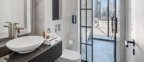 A modern bathroom with a large white sink, a toilet, and a glass-enclosed shower.