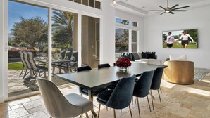 A spacious dining area with a large table, modern chairs, and a television mounted on the wall.