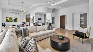 A spacious living room with a large sofa, a coffee table, and a dining area in the background.