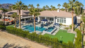 A resort with a swimming pool, lounge chairs, palm trees, and a mountain backdrop.