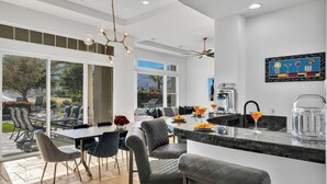A modern kitchen with a large island, dining area with chairs, and a view of the outdoors.