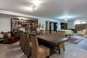 A spacious living room with a large wooden dining table surrounded by wicker chairs, a bookshelf filled with books, and a fireplace. - Villa Nicolas (Κynopiastes)