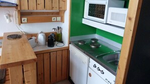 A compact kitchen with wooden cabinets, a microwave, a stove, and a sink.