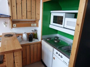 A compact kitchen with wooden cabinets, a microwave, a stove, and a sink.
