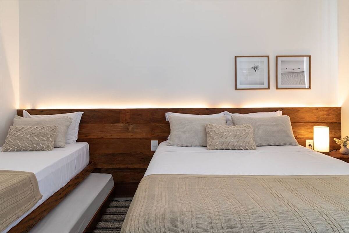 Ein Hotelzimmer mit zwei Betten, Holz-Kopfteilen, weißer Bettwäsche und zwei gerahmten Bildern an der Wand.
