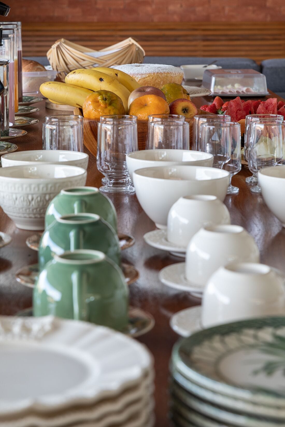 Une table à manger dressée avec différents bols, tasses et un panier de fruits.