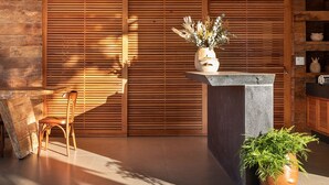 Un interior moderno con pared de listones de madera, mostrador de recepción de piedra, una silla de madera y una planta en maceta.