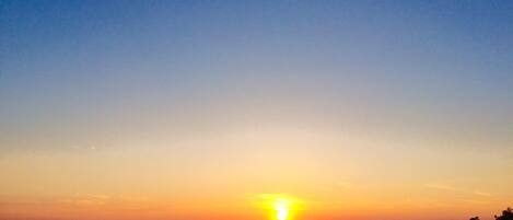 A sunset over a calm body of water with distant landforms.
