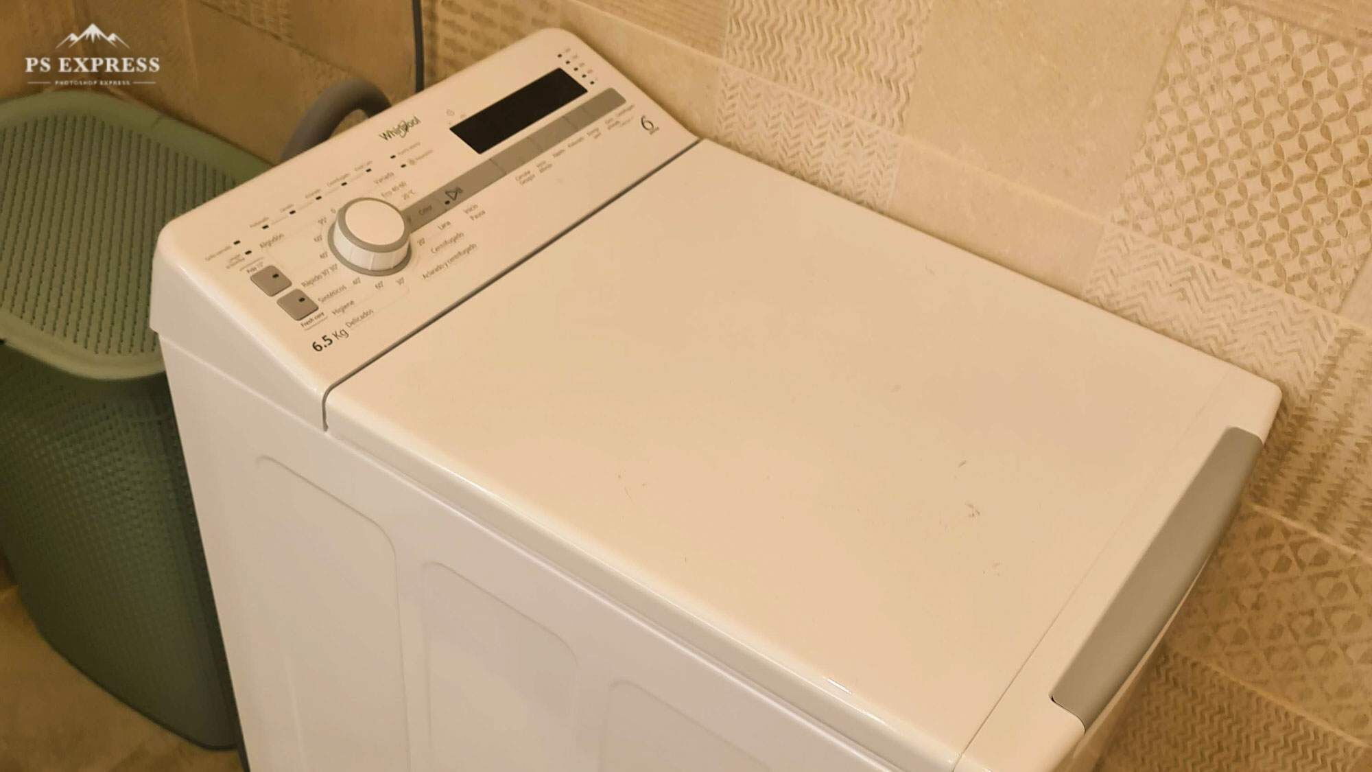 A front view of a white Whirlpool washing machine with a control panel, located in a bathroom with patterned tiles.