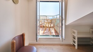 Ein Zimmer mit großem Fenster, Holzboden, einem Stuhl und einem weißen Regal.
