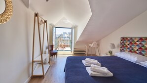 Ein Schlafzimmer mit einem großen Bett, Blick auf die Stadt, einer Holzleiter und einem farbenfrohen geometrischen Wanddesign.