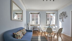 A living room with a blue sofa, a dining area with a round table and chairs, and a large mirror on the wall.