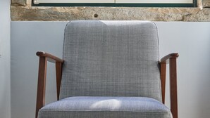 A chair with a woven backrest and wooden legs, positioned in front of a window with a view of a building with a tiled roof.