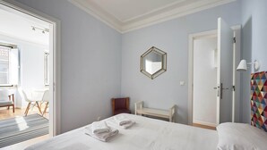 A hotel room with a bed, a chair, a small table, and a door.