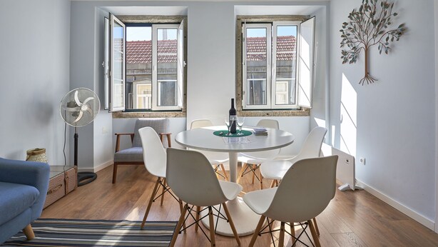 A dining area with a round table, white chairs, and a fan.