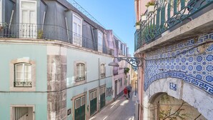 A narrow street with buildings featuring balconies, a cobblestone path, and a blue-tiled archway.