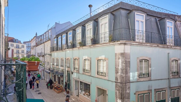 A narrow street with buildings on either side, featuring balconies with railings and windows.