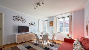 A modern bedroom with a large bed, a TV on a wooden cabinet, a dining table with chairs, and bicycles mounted on the wall.