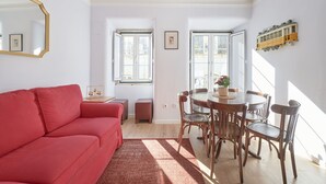 A modern living room with a red sofa, wooden dining table, and chairs, large windows, and a ceiling light fixture.