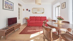 A modern living room with a red sofa, wooden entertainment unit, and a dining table with chairs.