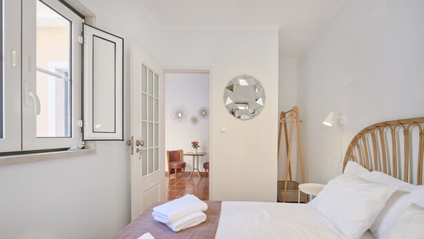 A hotel room with a bed, a bedside table, a mirror, and a door leading to a bathroom.