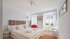 Une chambre à coucher comprenant un lit, une chaise, une chaise rouge, une petite table et une porte donnant sur un balcon.