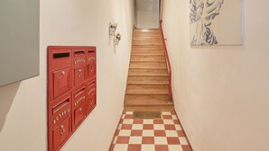 Un escalier avec un sol à carreaux, une boîte aux lettres rouge et un tableau accroché au mur.