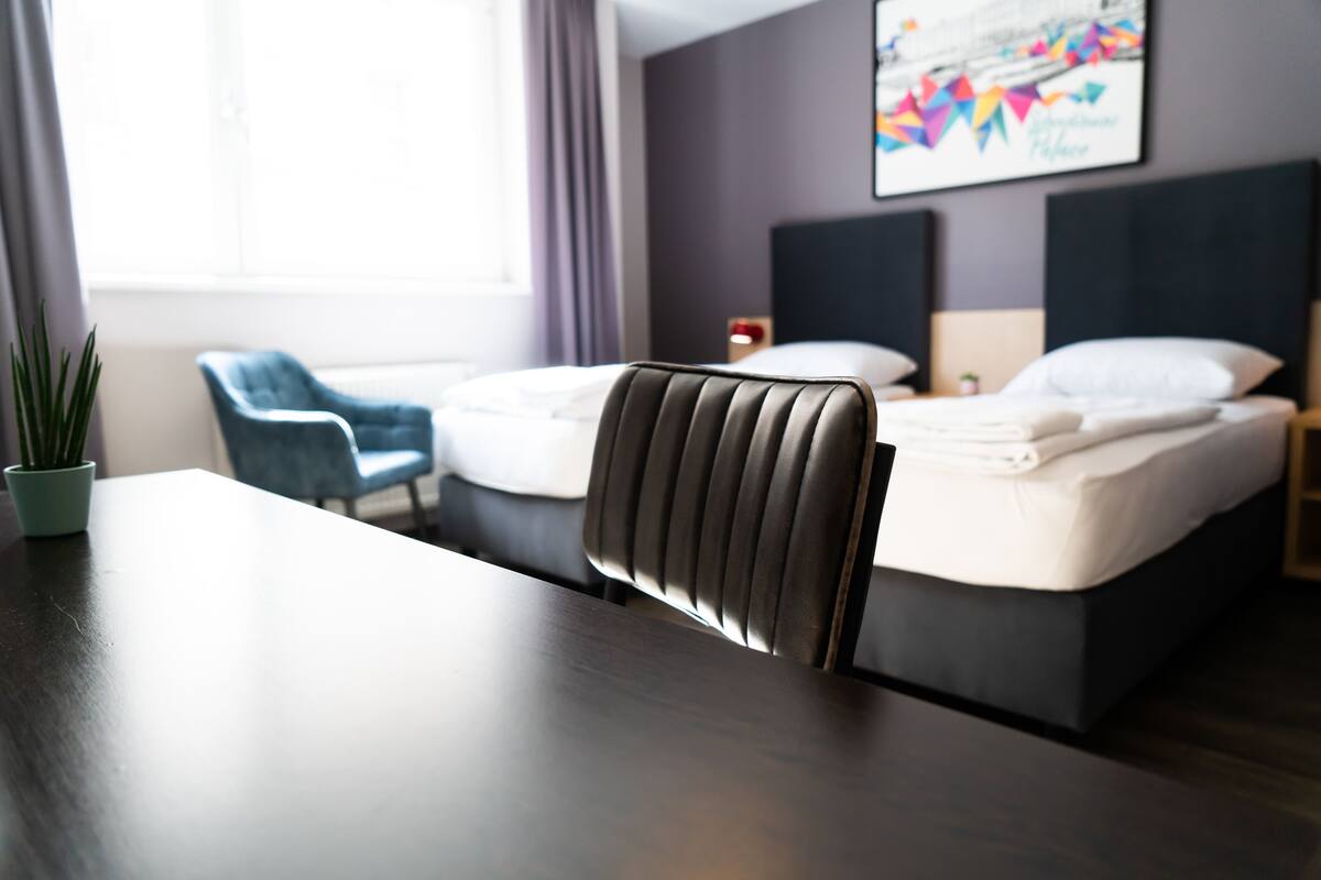 A hotel room with a bed, a chair, a table, and a window with curtains.