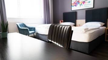 A hotel room with a bed, a chair, a table, and a window with curtains.