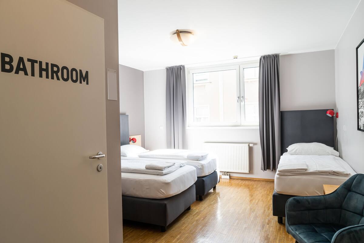 A hotel room with two beds, a dark headboard, a grey couch, and a window with curtains.
