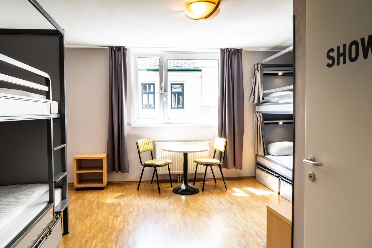 A compact room with bunk beds, a small table with chairs, a window with curtains, and a door labeled "SHOW".
