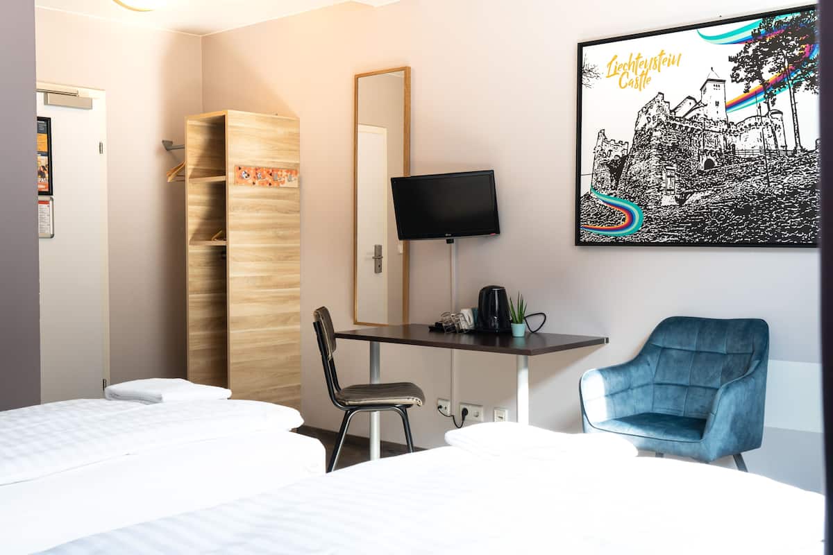 A hotel room with two beds, a desk with a chair, a TV, and a framed picture of a castle.