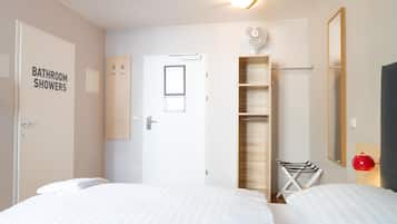 Ein Hotelzimmer mit zwei Betten, einem Badezimmer mit Duschen, einer Holzablage, einem Ventilator, einem roten Licht und einem Spiegel.