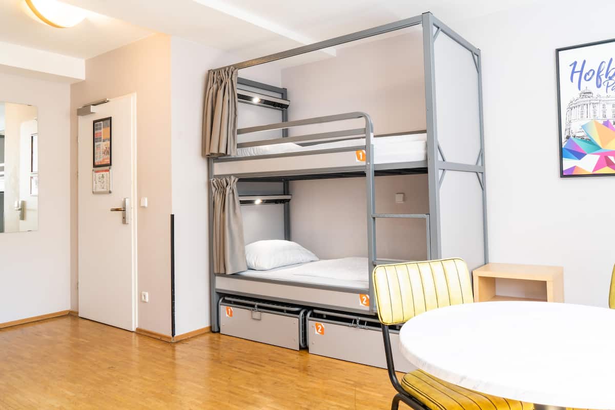 A bunk bed with storage drawers, a small table, and a chair in a room with wooden flooring and a door.
