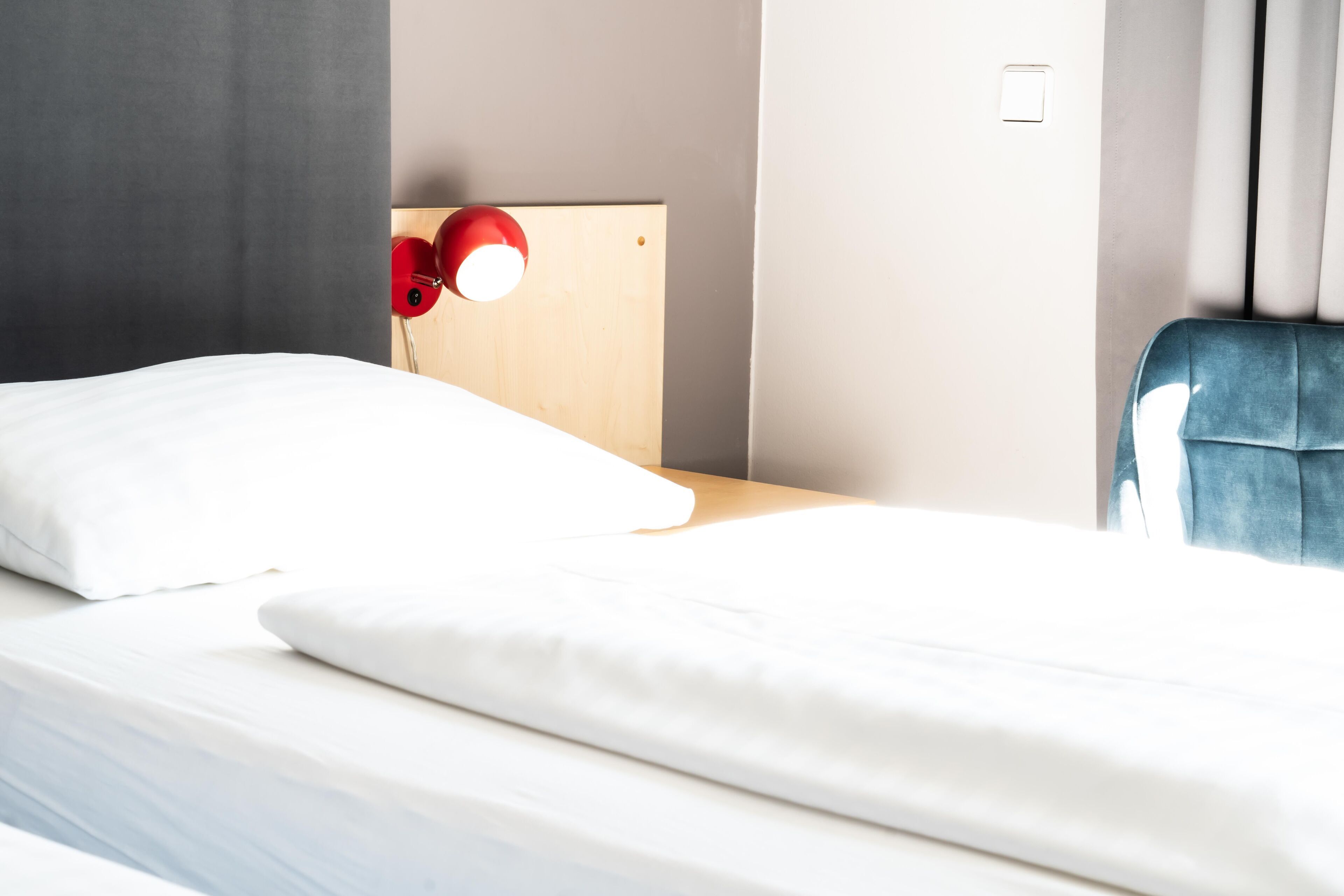 Una habitación de hotel con una cama, un cabecero de madera, una lámpara roja y una silla azul.