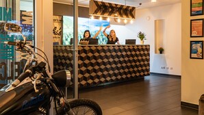 A reception area with a checkered wall pattern, a reception desk, and a motorcycle in the foreground. - St Christopher's Vienna - Hostel (Vienna)