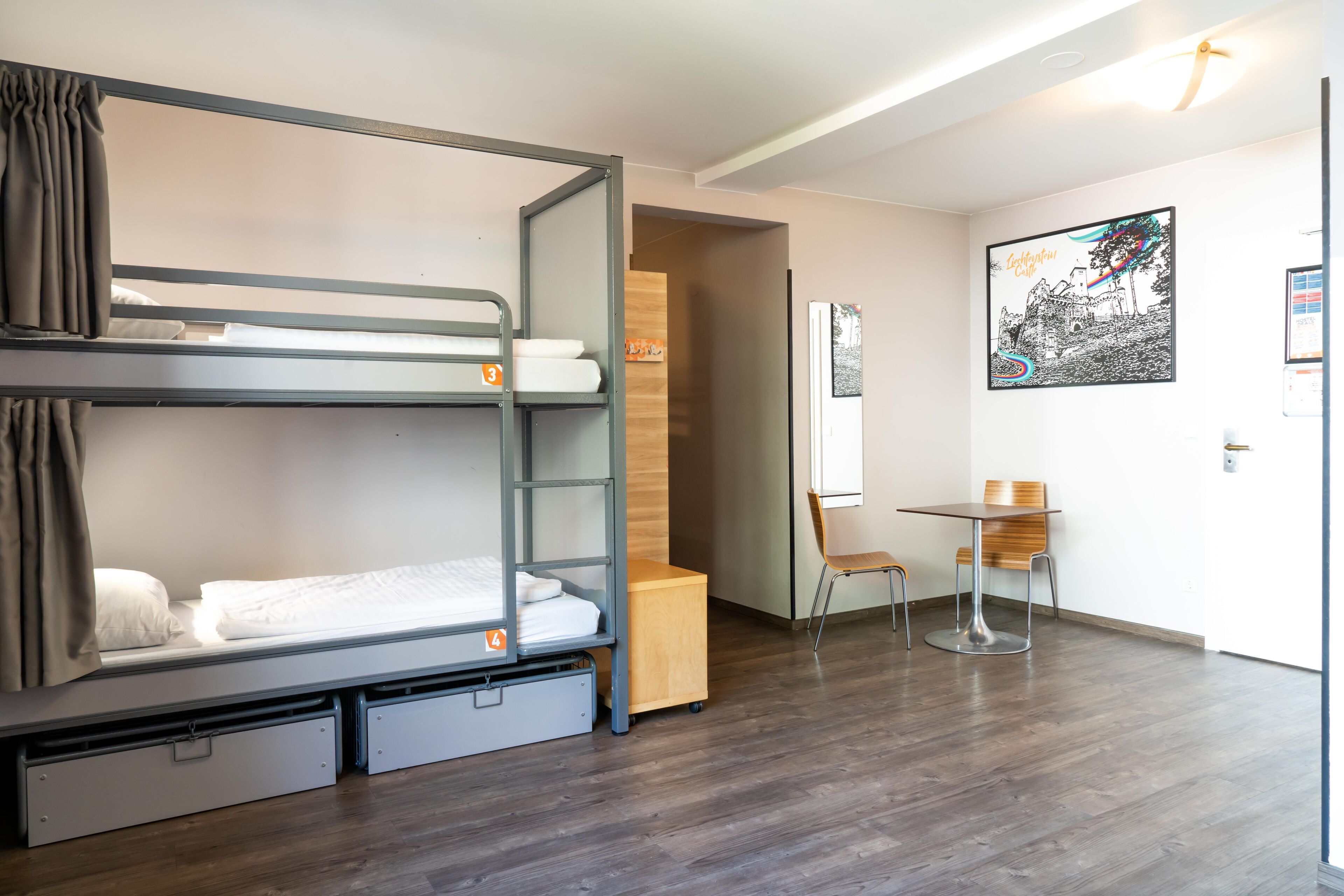 A bunk bed room with a desk and chair, a wooden cabinet, and a framed picture on the wall.