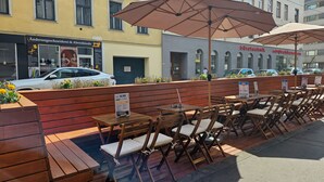 Outdoor seating with wooden tables and chairs, umbrellas, and a sign for 'The Food' restaurant. - St Christopher's Vienna - Hostel (Vienna)