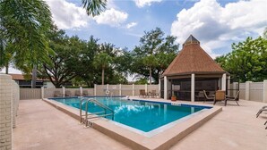 A rectangular swimming pool with a tiled deck, surrounded by a wooden fence and trees. - Gulf Gate - Quaint and fresh 1st floor condo w/covered parking (Sarasota)