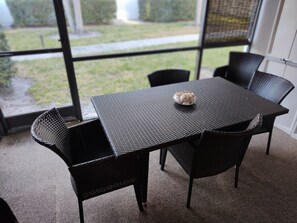 Un coin repas avec une table et des chaises, un bol de nourriture, et une vue sur un jardin grâce à de grandes fenêtres.