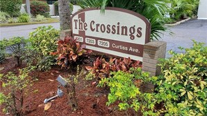 A sign for 'The Crossings' with three phone numbers and the address 'Curtiss Ave.' - Gulf Gate - Quaint and fresh 1st floor condo w/covered parking (Sarasota)